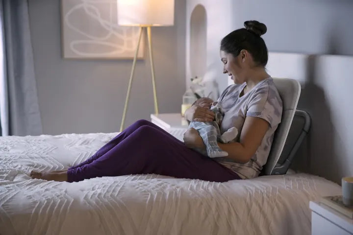 A mother holding her baby in bed, leaning on the Ready Rocker